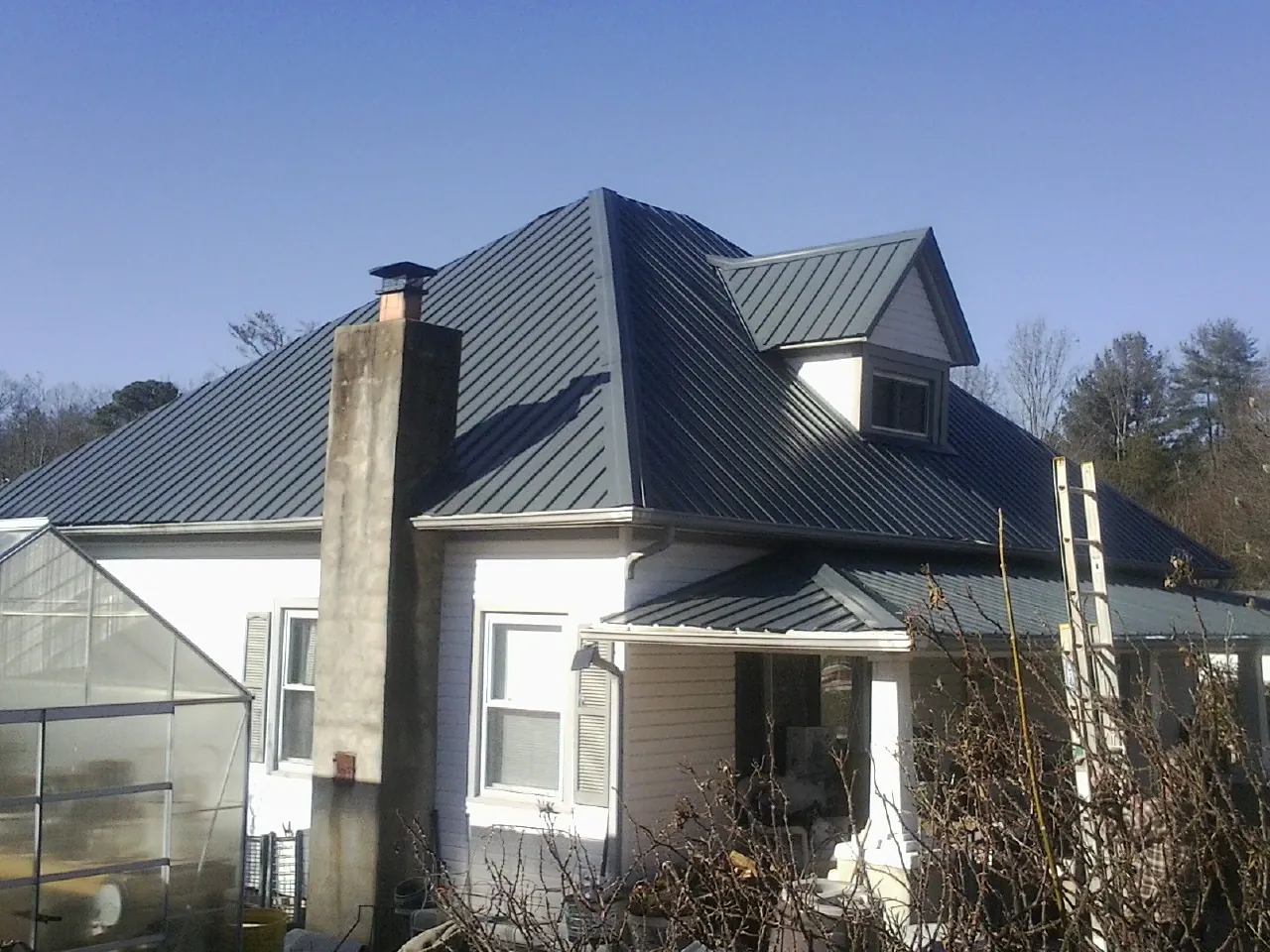 Dark blue standing seam metal roof on a white farmhouse with dormer — Slate & Tile Roof Repair by Roofing Brothers in Osseo