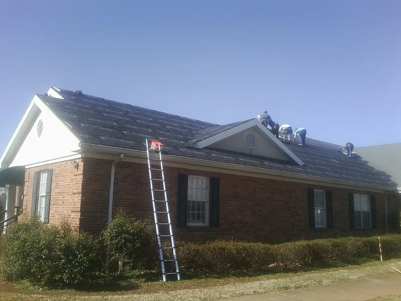 Crew tearing shingles off a brick ranch roof with a ladder set — Emergency Roof Repair work by our crew in Osseo