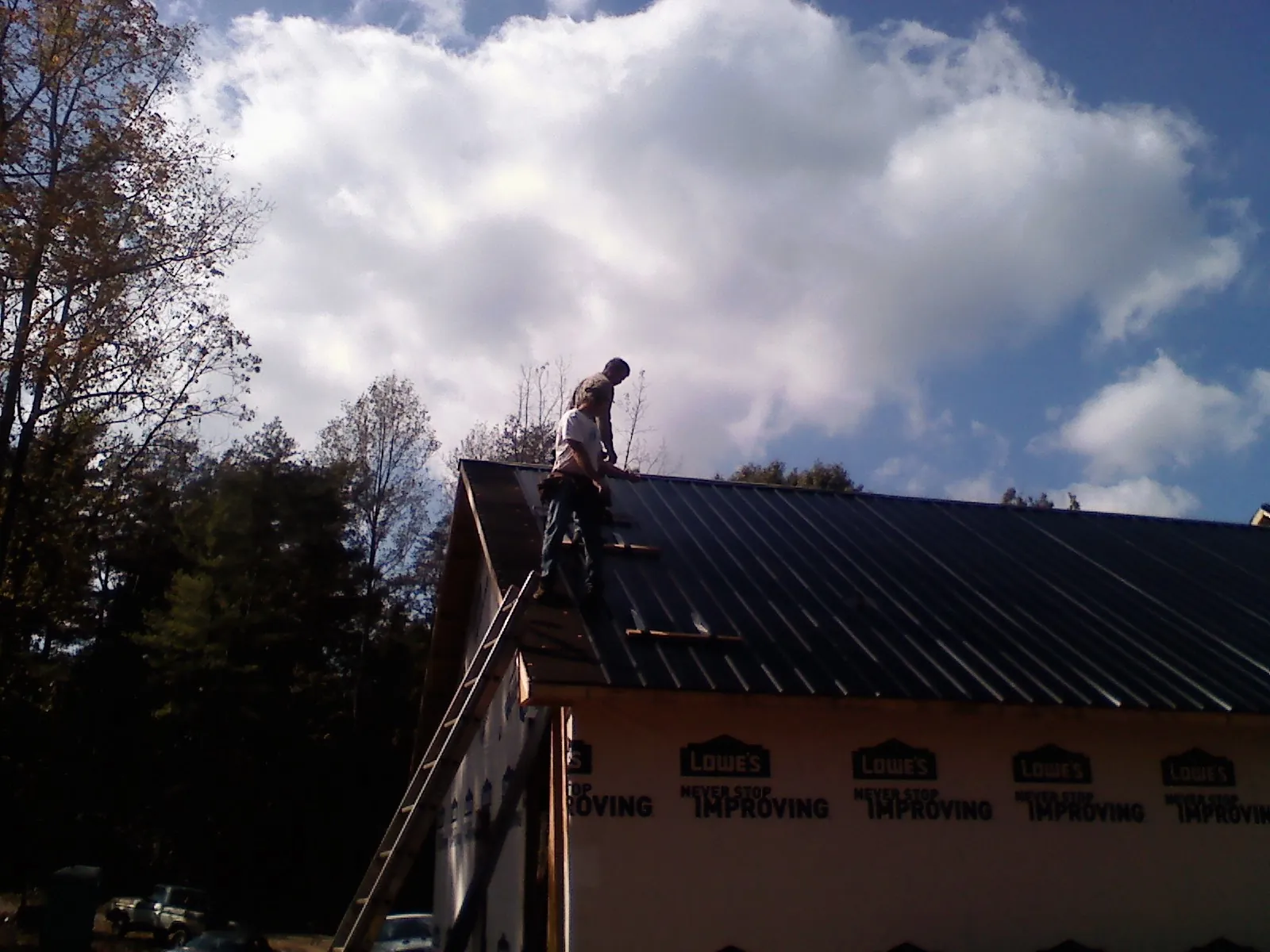 Roofer fastening dark metal panels high against a cloudy sky, from a Roof Inspection job in Osseo