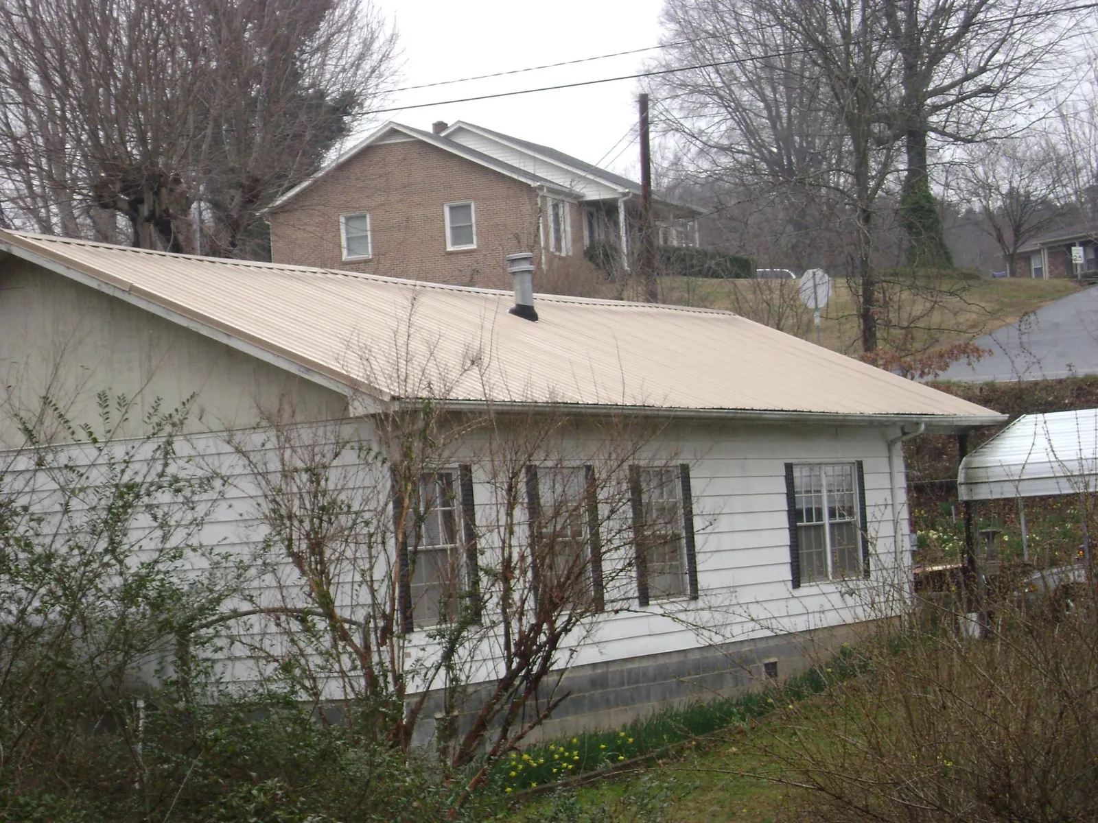 Tan metal roof on a white sided house set into a hillside — Commercial Roofing by Roofing Brothers in Osseo